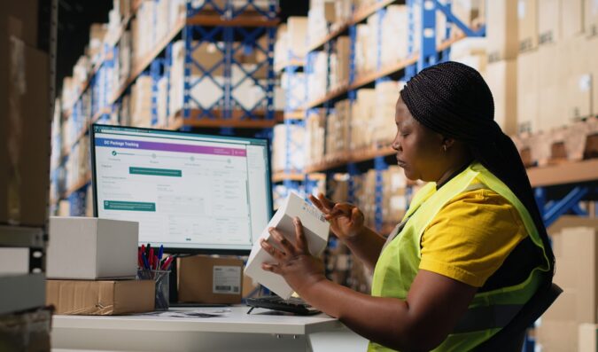 Woman staff managing package labeling using shipment details adhesive tags, handling order processing and preparing the packages for distribution. Online shopping fulfillment center. Camera B.
